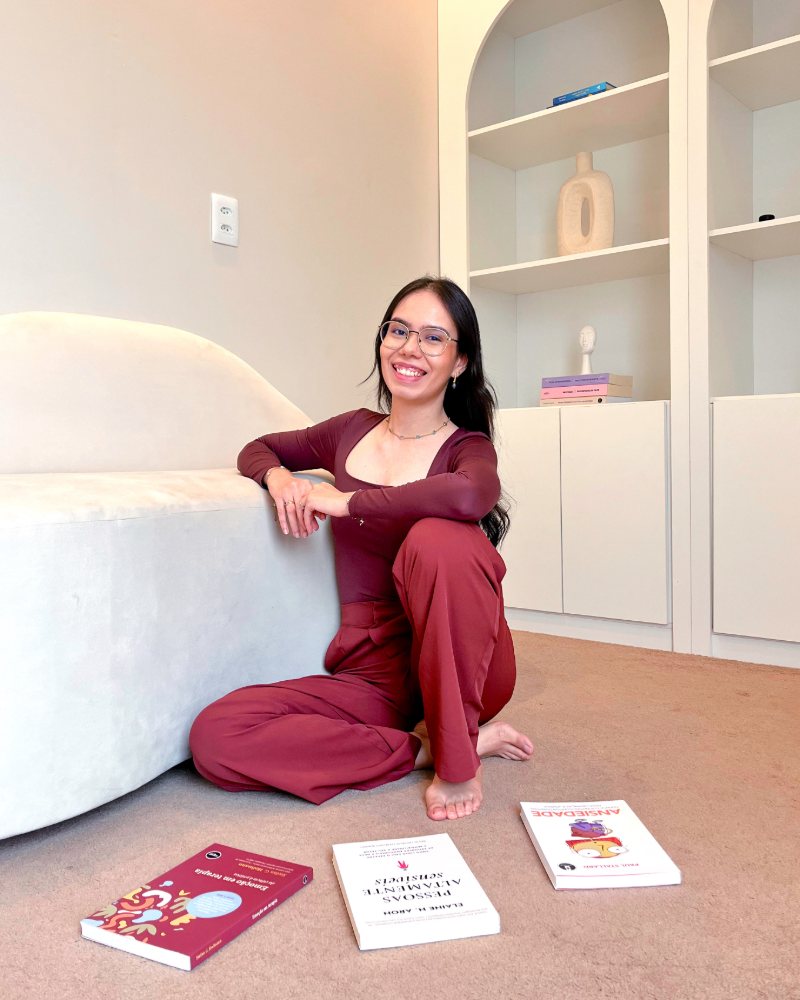 Fernanda Manuela, psicóloga, sentada no chão do consultório ao lado de livros sobre ansiedade e emoções