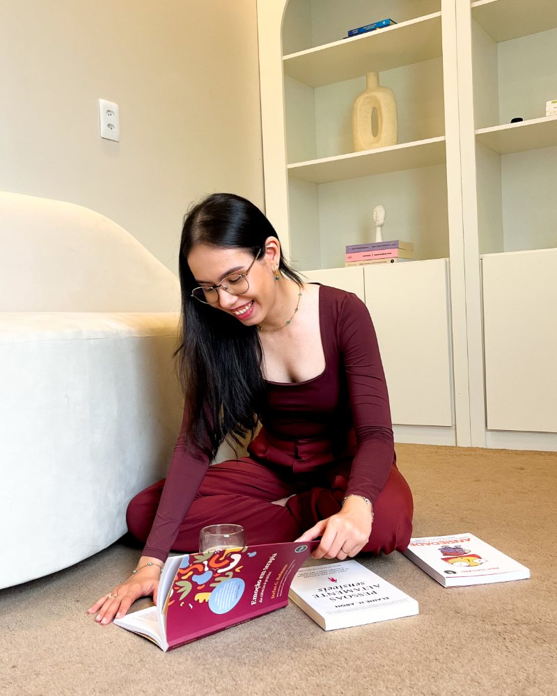 Fernanda Manuela, psicóloga, sentada no tapete do consultório folheando livros sobre emoções e ansiedade